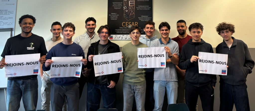 Group of students standing in a classroom, each holding a sign that reads 'REJOINS-NOUS'.