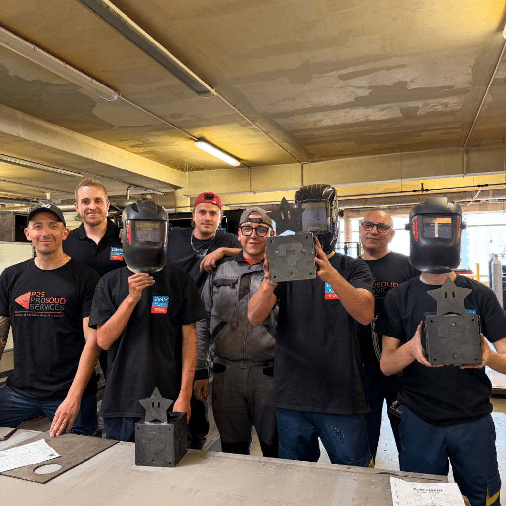 Group of seven welders in a workshop, some wearing helmets, posing with metal star sculptures and blocks.